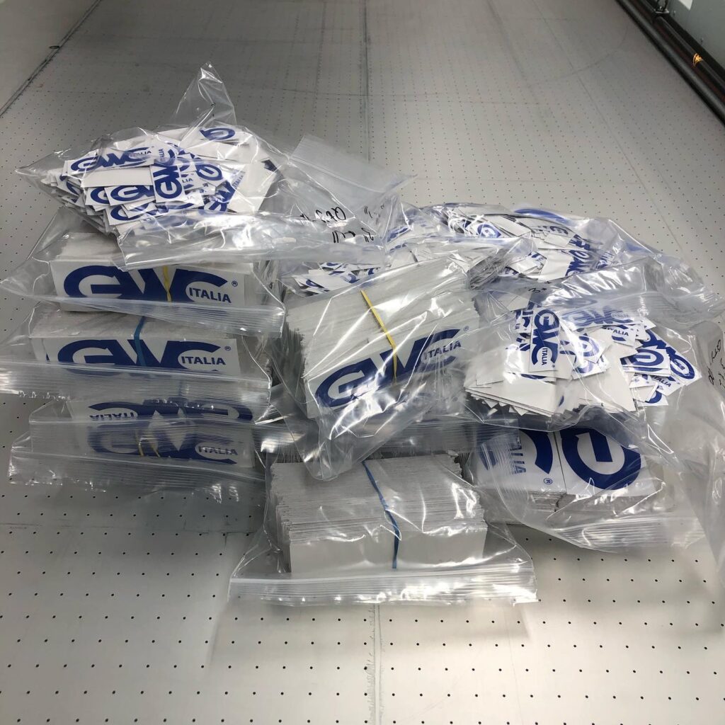 Stacks of packaged promotional stickers featuring the logo "GV ITALIA," illustrating custom branding options offered by Elite Signs LLC.