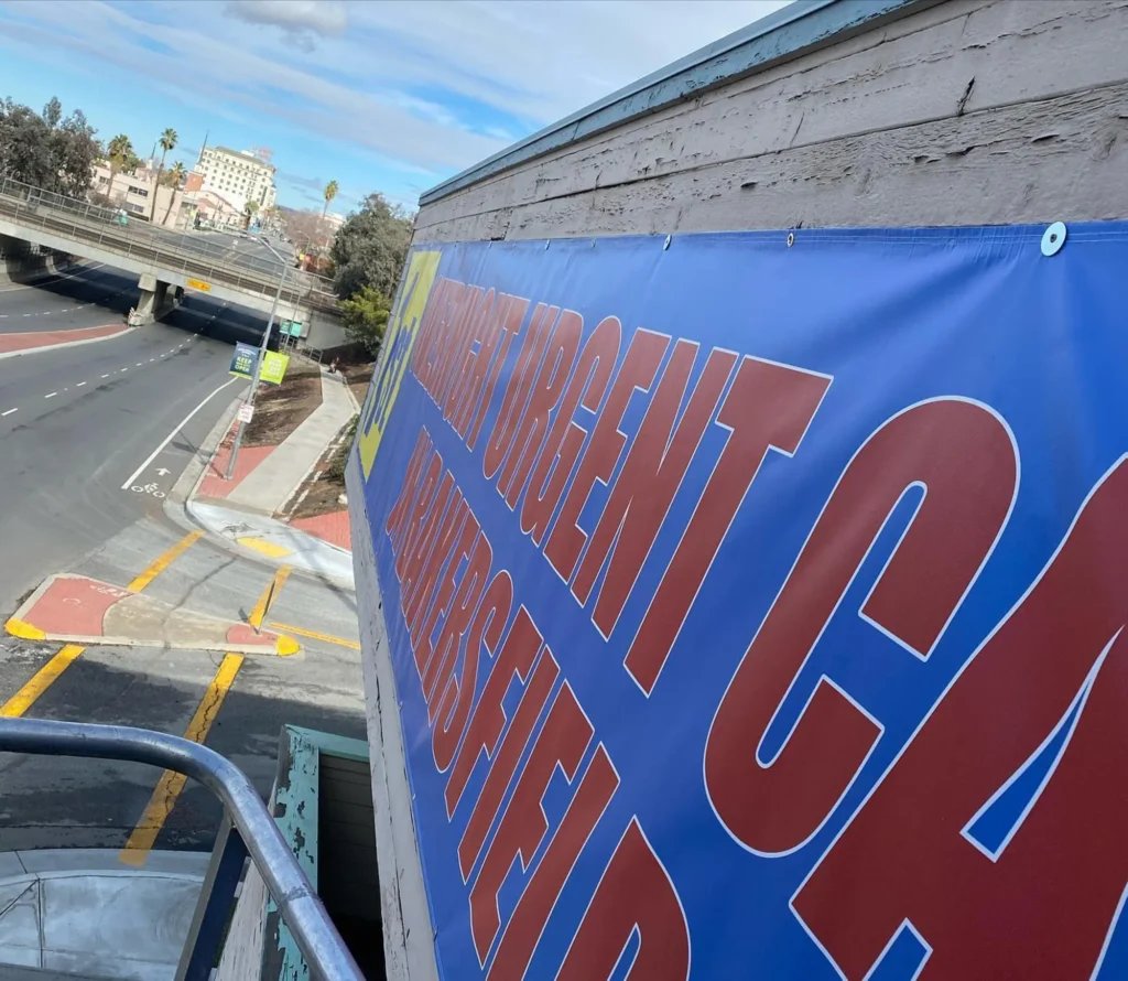 Banner advertising urgent care services in Bakersfield, featuring bold text and vibrant colors, positioned above a road for high visibility.