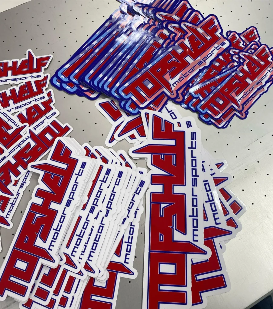 Custom decals featuring "TOP SHELF motorsports" logo in red and blue, showcasing high-quality design for branding applications.