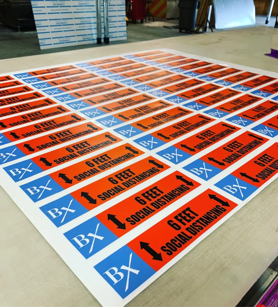 Custom social distancing decals printed on orange and blue backgrounds, featuring the text "6 FEET SOCIAL DISTANCING" and directional arrows, showcasing Elite Signs LLC's decal craftsmanship.