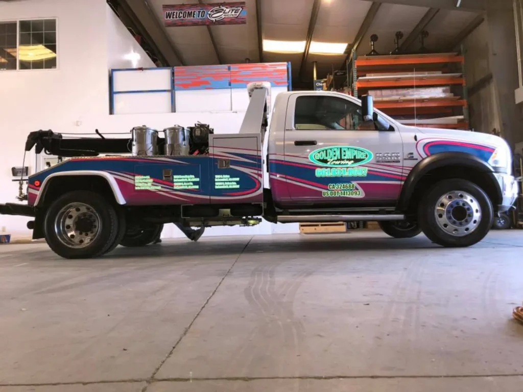 Tow truck with vibrant custom decals featuring "Golden Empire Towing" branding, parked indoors showcasing high-quality design and craftsmanship.