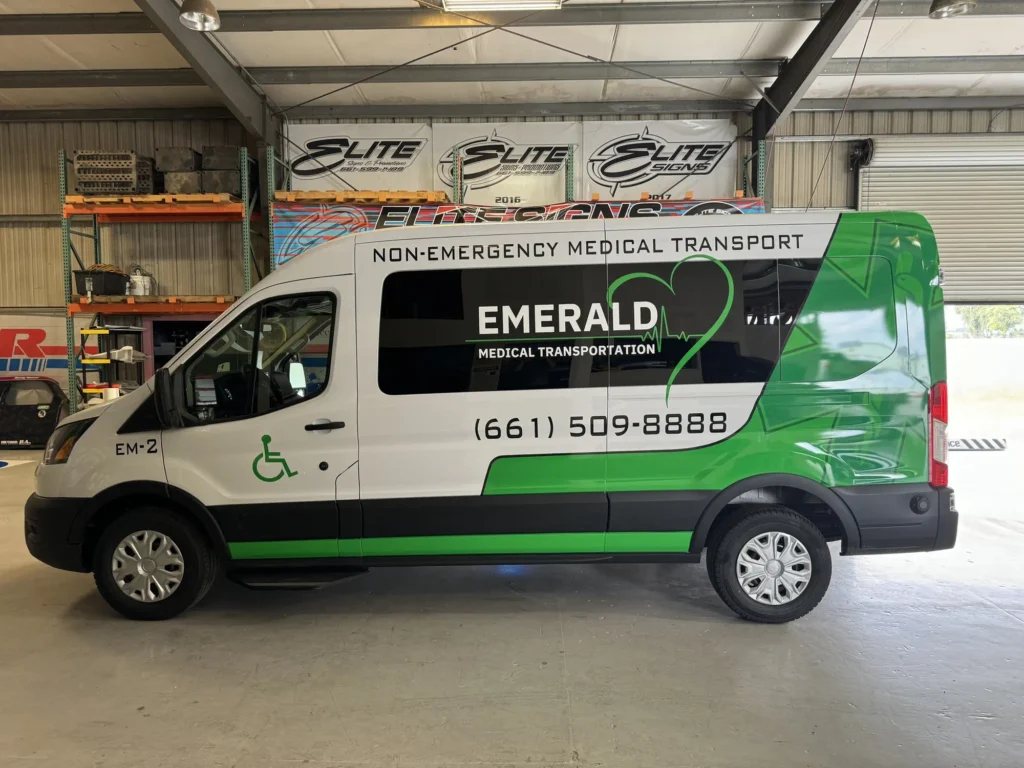 Custom vehicle wrap for Emerald Medical Transportation featuring vibrant green and white design, showcasing branding and contact information, inside Elite Signs workshop.