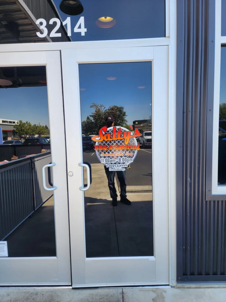 Salty's BBQ & Catering logo and business hours vinyl decal on a storefront glass door in Bakersfield, CA