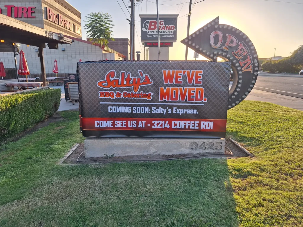 Salty's BBQ & Catering custom vinyl We've Moved banner on a monument sign announcing the new Coffee Rd location in Bakersfield, CA